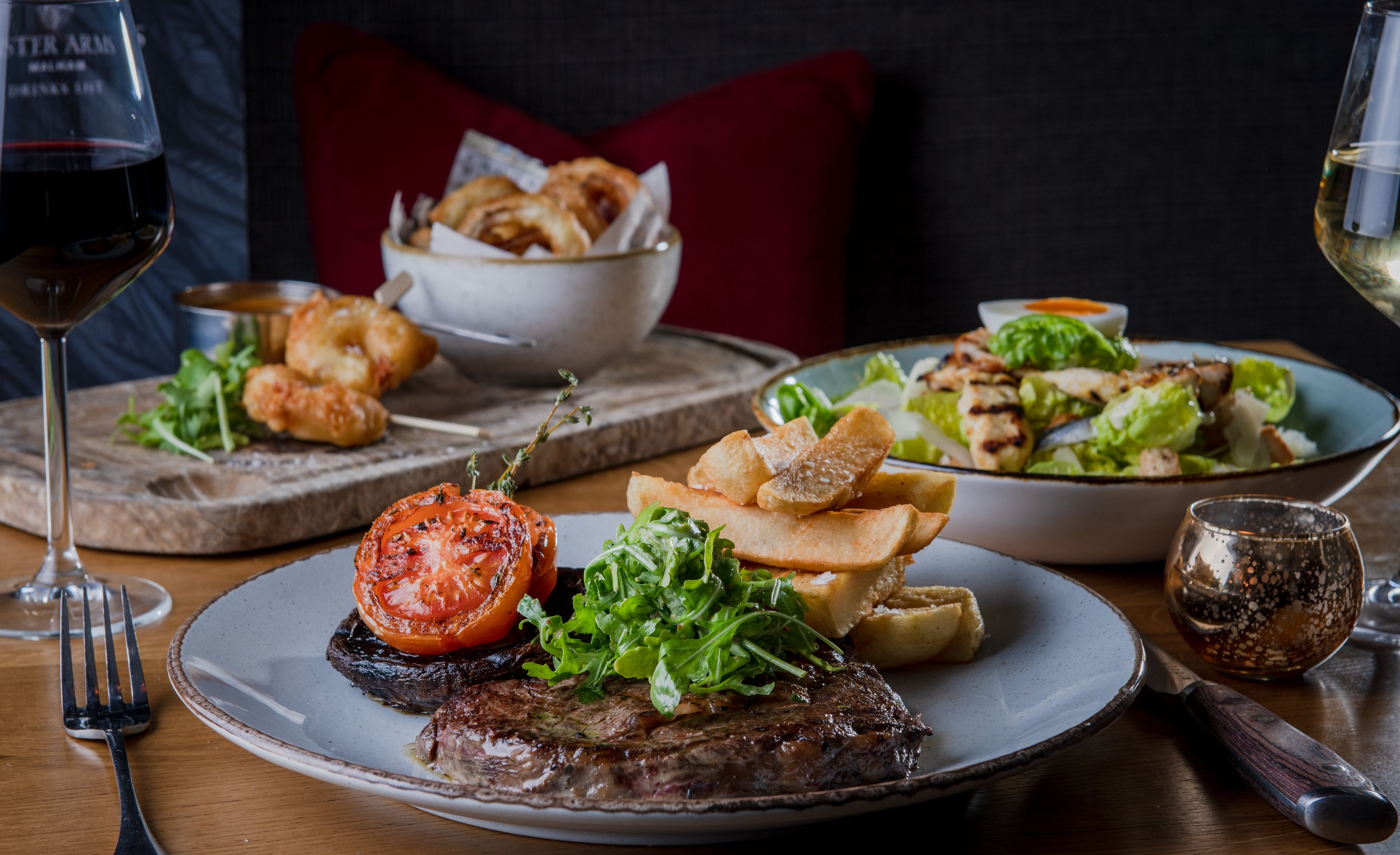 steak, chips, mushroom and tomatoes with caesar salad, tempura prawns and wine on a table